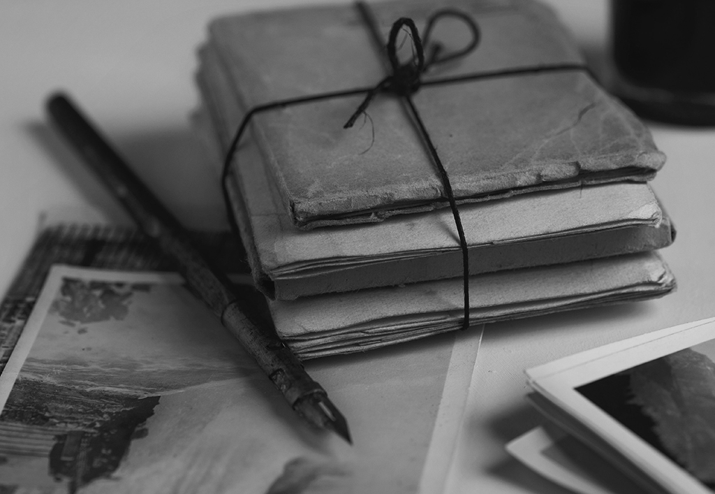 closeup image of a bundle of letters, old photos, and a pen